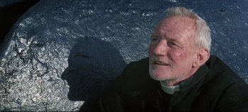 Movie still from “Ryan's Daughter” (1970), directed by David Lean – An older man wearing a priest's collar and standing in front of a rock wall; Close Up shot, Low angle