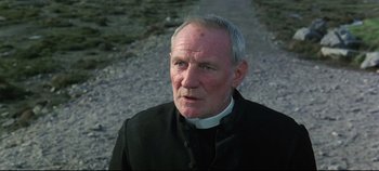 Movie still from “Ryan's Daughter” (1970), directed by David Lean – An older man wearing a priest's collar and standing on the side of a road; Close Up shot, Low angle