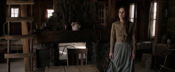 Movie still from “Godless” (2017), directed by Scott Frank – A woman standing in front of a stone fireplace; Medium shot, Low angle