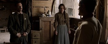 Movie still from “Godless” (2017), directed by Scott Frank – A woman standing in front of a wooden cabinet in a room; Medium shot, Over the shoulder angle