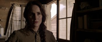 Movie still from “Godless” (2017), directed by Scott Frank – A woman with a braid standing in front of a window; Close Up shot, Over the shoulder angle