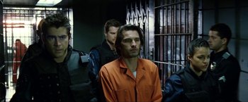 Movie still from “S.W.A.T.” (2003), directed by Clark Johnson – A man in an orange shirt is in a jail cell; Medium shot, Over the shoulder angle