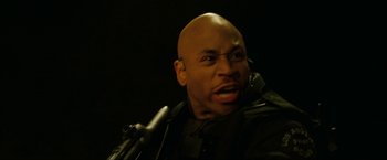 Movie still from “S.W.A.T.” (2003), directed by Clark Johnson – A bald man with a microphone in front of a microphone stand; Close Up shot, Low angle