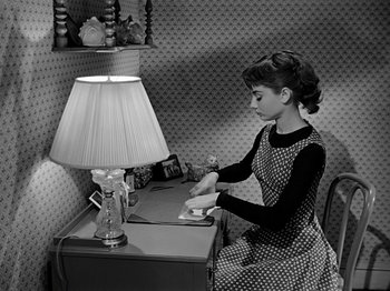 Movie still from “Sabrina” (1954), directed by Billy Wilder – A woman sitting at a desk with a cup of coffee; Medium shot, High angle