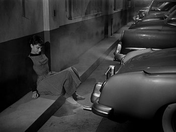 Movie still from “Sabrina” (1954), directed by Billy Wilder – A woman sitting on the ground next to a row of parked cars; Wide shot, High angle