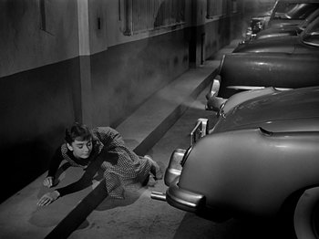 Movie still from “Sabrina” (1954), directed by Billy Wilder – A man is laying on the ground next to a row of parked cars; Wide shot, High angle