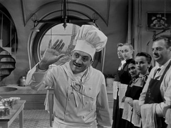 Movie still from “Sabrina” (1954), directed by Billy Wilder – A man in a chef's hat waving to the camera; Medium shot, Low angle