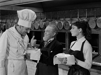 Movie still from “Sabrina” (1954), directed by Billy Wilder – A man and two women are in a kitchen; Medium shot, High angle