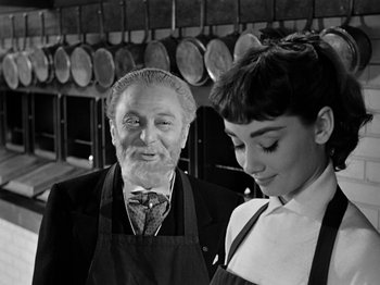 Movie still from “Sabrina” (1954), directed by Billy Wilder – An old man and a young woman standing in front of a row of pans; Close Up shot, Over the shoulder angle