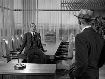 Movie still from “Sabrina” (1954), directed by Billy Wilder – A man in a suit and a hat sitting in front of another man in a hat; Wide shot, Over the shoulder angle