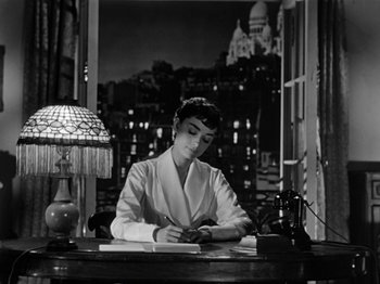 Movie still from “Sabrina” (1954), directed by Billy Wilder – A woman sitting at a desk writing on a piece of paper; Medium shot, High angle