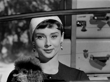 Movie still from “Sabrina” (1954), directed by Billy Wilder – A woman holding a small dog in her arms; Close Up shot, Low angle