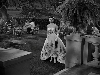 Movie still from “Sabrina” (1954), directed by Billy Wilder – A woman in a long dress standing in a yard; Wide shot, High angle