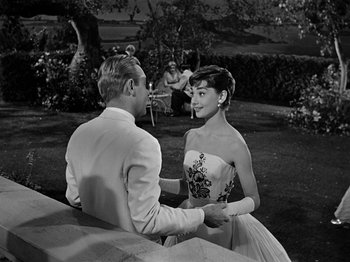 Movie still from “Sabrina” (1954), directed by Billy Wilder – A man and a woman holding hands in front of a tree; Medium shot, Over the shoulder angle