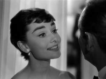 Movie still from “Sabrina” (1954), directed by Billy Wilder – A black - and - white photo of a woman smiling at a man; Close Up shot, Over the shoulder angle