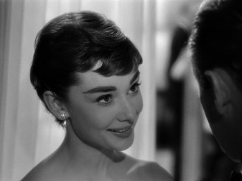 Movie still from “Sabrina” (1954), directed by Billy Wilder – A black - and - white photo of a woman smiling; Close Up shot, Over the shoulder angle