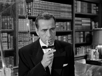 Movie still from “Sabrina” (1954), directed by Billy Wilder – A man in a suit smoking a cigarette in a library; Medium shot, Low angle