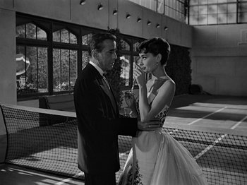 Movie still from “Sabrina” (1954), directed by Billy Wilder – A man and a woman standing next to each other on a tennis court; Medium shot, Low angle