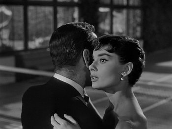 Movie still from “Sabrina” (1954), directed by Billy Wilder – A man and a woman embracing each other in front of a building; Close Up shot, Low angle