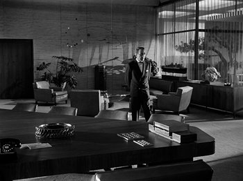 Movie still from “Sabrina” (1954), directed by Billy Wilder – A black and white photo of a man in a suit and tie in a room; Wide shot, Low angle