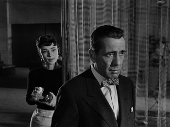 Movie still from “Sabrina” (1954), directed by Billy Wilder – A man and a woman standing next to each other in a room; Medium shot, Over the shoulder angle