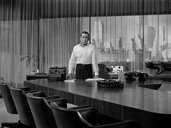 Movie still from “Sabrina” (1954), directed by Billy Wilder – A black and white photo of a man standing in front of a desk; Wide shot, Low angle