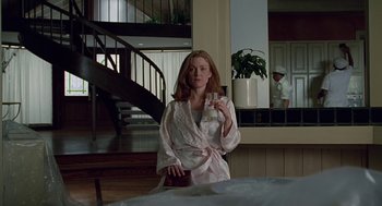 Movie still from “Safe” (1995), directed by Todd Haynes – A woman sitting in front of a table holding a glass; Medium shot, Low angle