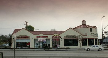 Movie still from “Safe” (1995), directed by Todd Haynes – A white store front with many signs on the side of the building; Extreme Wide shot, Low angle