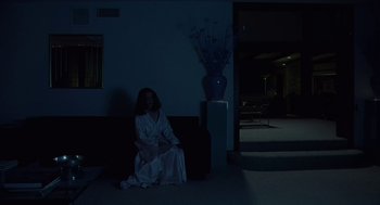 Movie still from “Safe” (1995), directed by Todd Haynes – A woman sitting on a couch in a dark room; Wide shot, Low angle