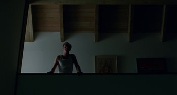 Movie still from “Safe” (1995), directed by Todd Haynes – A man sitting on top of a table in a dark room; Wide shot, Low angle