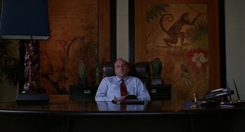 Movie still from “Safe” (1995), directed by Todd Haynes – A man sitting at a desk in front of a painting; Medium shot, Low angle