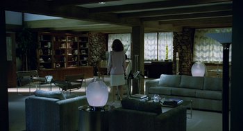 Movie still from “Safe” (1995), directed by Todd Haynes – A woman is standing in a living room with furniture; Wide shot, High angle
