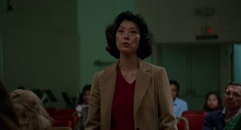 Movie still from “Safe” (1995), directed by Todd Haynes – A woman in a brown jacket standing in front of people; Close Up shot, Low angle