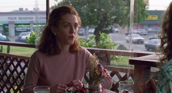 Movie still from “Safe” (1995), directed by Todd Haynes – A woman sitting at a table with a vase of flowers in front of her; Medium shot, Over the shoulder angle