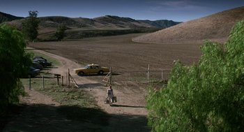 Movie still from “Safe” (1995), directed by Todd Haynes – A man walking down a dirt road near a car; Extreme Wide shot, High angle