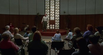 Movie still from “Safe” (1995), directed by Todd Haynes – A man standing in front of an audience in front of an audience; Wide shot, High angle