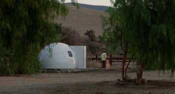 Movie still from “Safe” (1995), directed by Todd Haynes – A man standing in front of an object in the middle of a field; Extreme Wide shot, Low angle