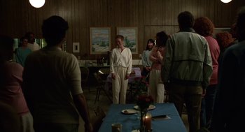 Movie still from “Safe” (1995), directed by Todd Haynes – A group of people standing around a table; Wide shot, Over the shoulder angle
