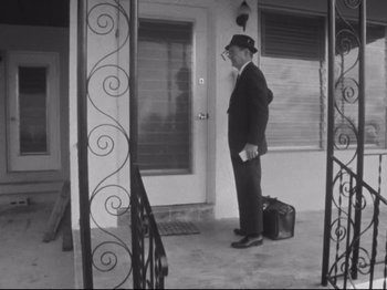 Movie still from “Salesman” (1969), directed by Albert Maysles – A black and white photo of a man standing on a porch; Wide shot, Low angle