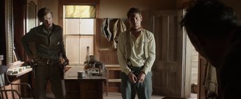 Movie still from “Godless” (2017), directed by Scott Frank – A man standing in front of a wooden table; Medium shot, Low angle