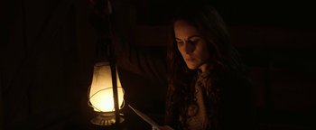 Movie still from “Godless” (2017), directed by Scott Frank – A woman reading a book in the dark with an oil lamp in the background; Close Up shot, Low angle