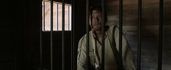 Movie still from “Godless” (2017), directed by Scott Frank – A man sitting behind bars in a jail cell; Medium shot, Low angle