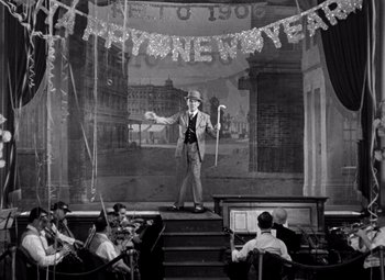 Movie still from “San Francisco” (1936), directed by W.S. Van Dyke – An old photo of a man on a stage with a microphone; Wide shot, High angle
