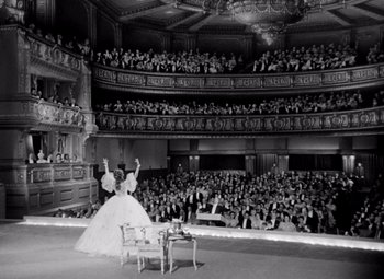 Movie still from “San Francisco” (1936), directed by W.S. Van Dyke – An old photo of a woman in a ball gown on a stage; Extreme Wide shot, High angle