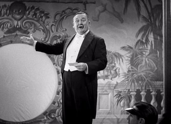Movie still from “San Francisco” (1936), directed by W.S. Van Dyke – A man in a tuxedo is holding an object in front of him; Medium shot, Low angle