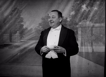 Movie still from “San Francisco” (1936), directed by W.S. Van Dyke – A man in a tuxedo is holding a cigarette; Medium shot, Low angle