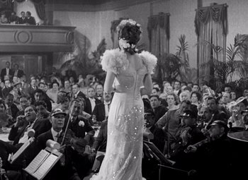 Movie still from “San Francisco” (1936), directed by W.S. Van Dyke – A woman in a white dress standing in front of an audience; Medium shot, Low angle