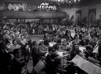 Movie still from “San Francisco” (1936), directed by W.S. Van Dyke – A large group of people sitting in a room; Extreme Wide shot, High angle