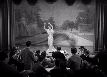 Movie still from “San Francisco” (1936), directed by W.S. Van Dyke – An old photo of a woman on a stage; Wide shot, High angle