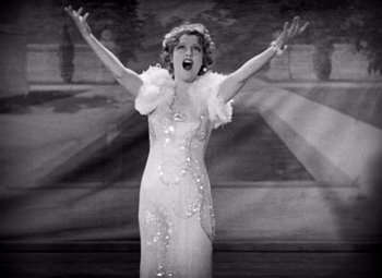 Movie still from “San Francisco” (1936), directed by W.S. Van Dyke – An old photo of a woman in a white dress; Medium shot, Low angle